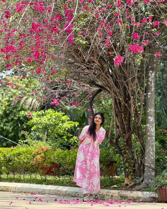Woman in a pink dress standing under a tree with pink flowers in a garden setting