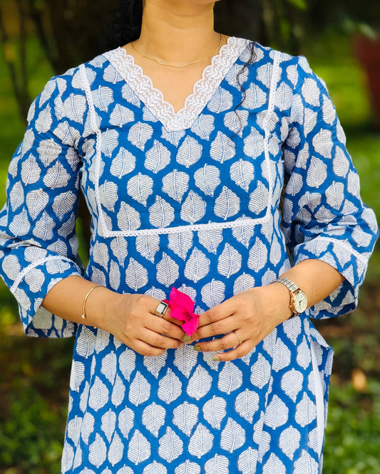Person wearing a blue and white patterned dress holding a pink flower against a blurred green background