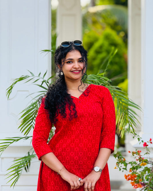 Woman in a red dress standing outdoors with greenery and white columns in the background