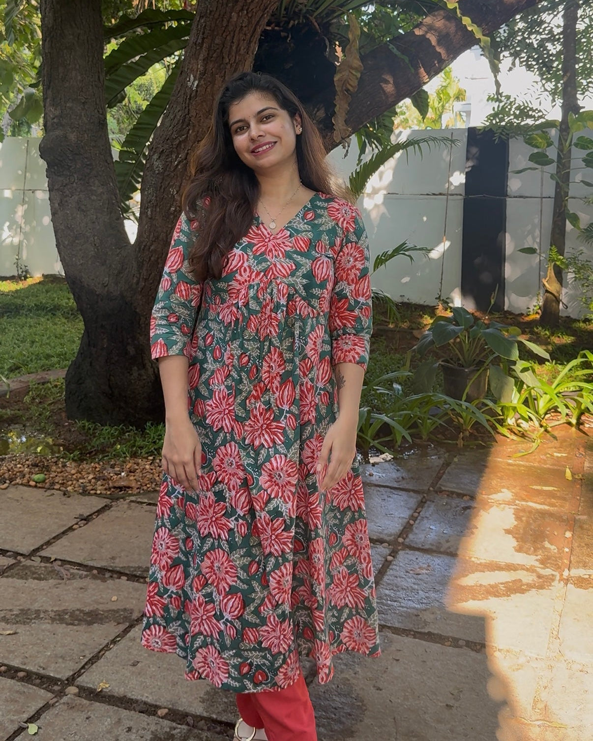 Woman in a floral dress standing outdoors near a tree