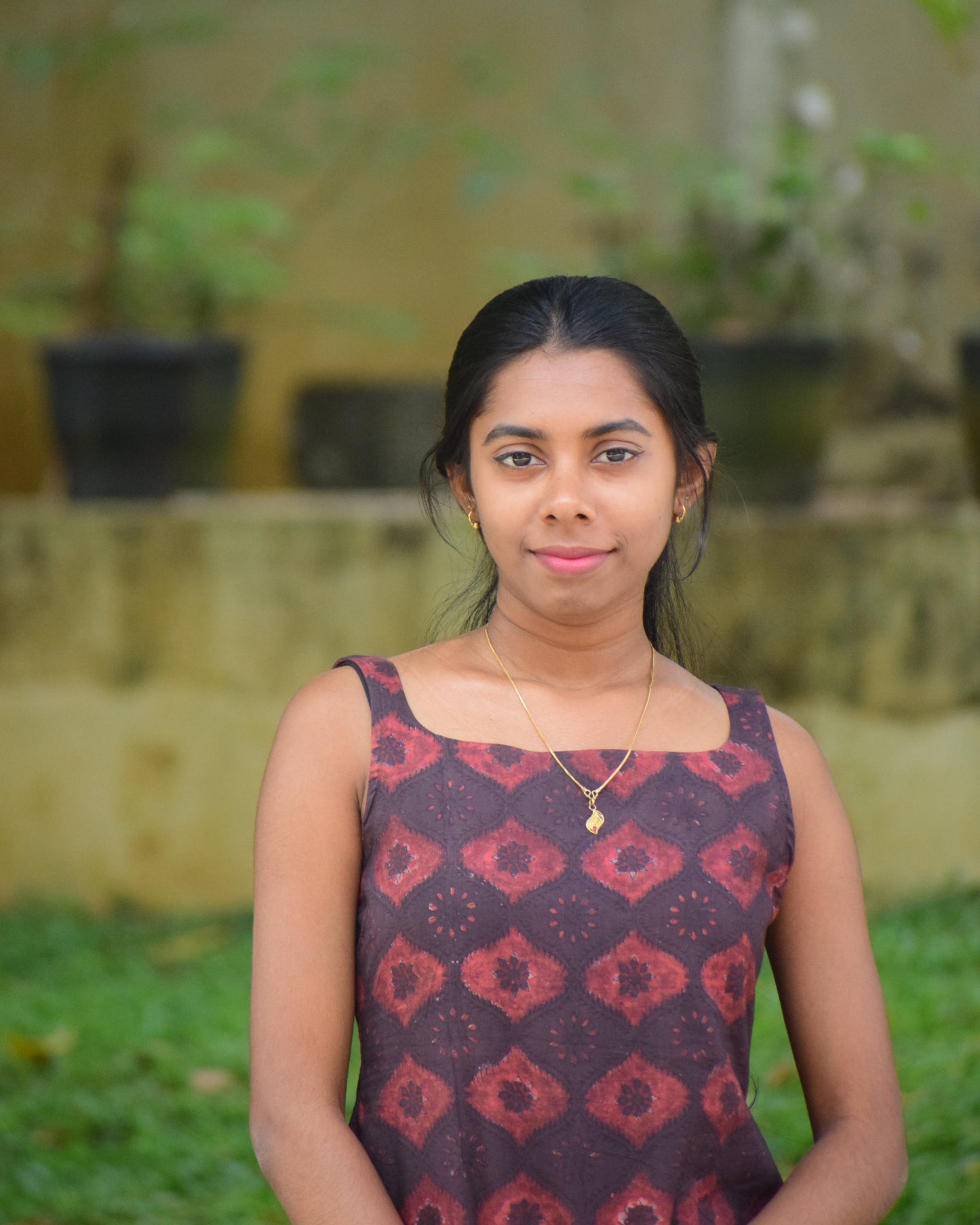 Woman wearing a patterned dress standing outdoors with greenery in the background