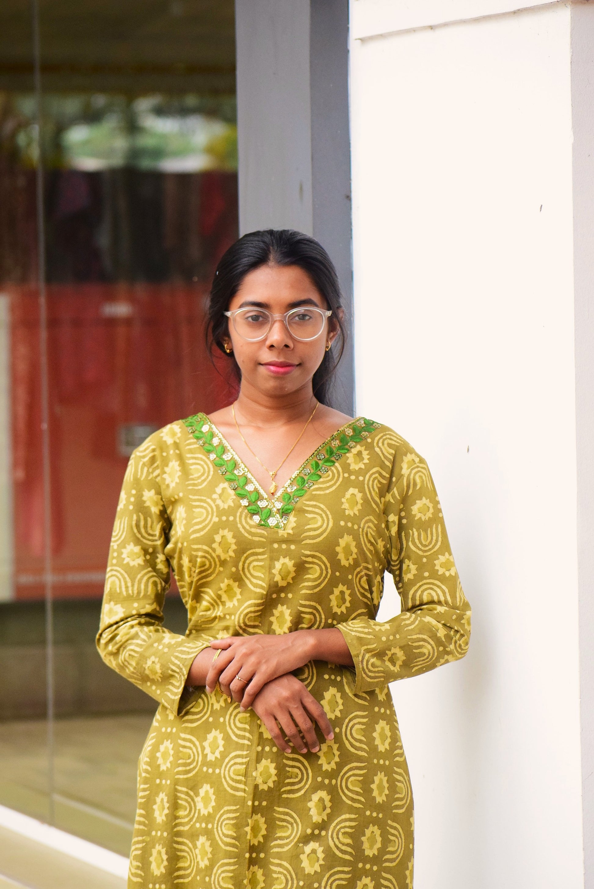 Woman wearing a yellow patterned dress with green accents, standing indoors.