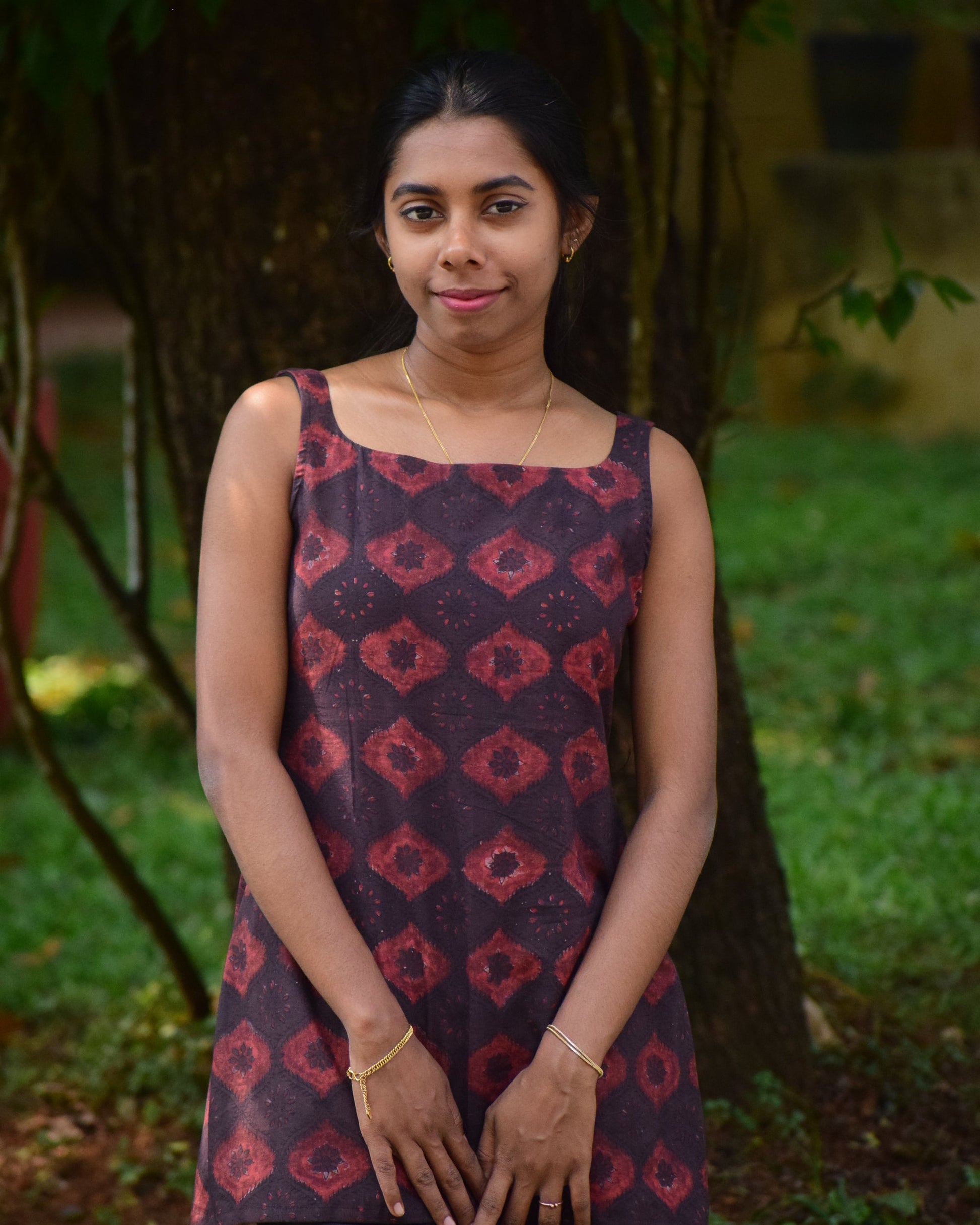 Woman in a patterned dress standing in a natural setting with greenery.