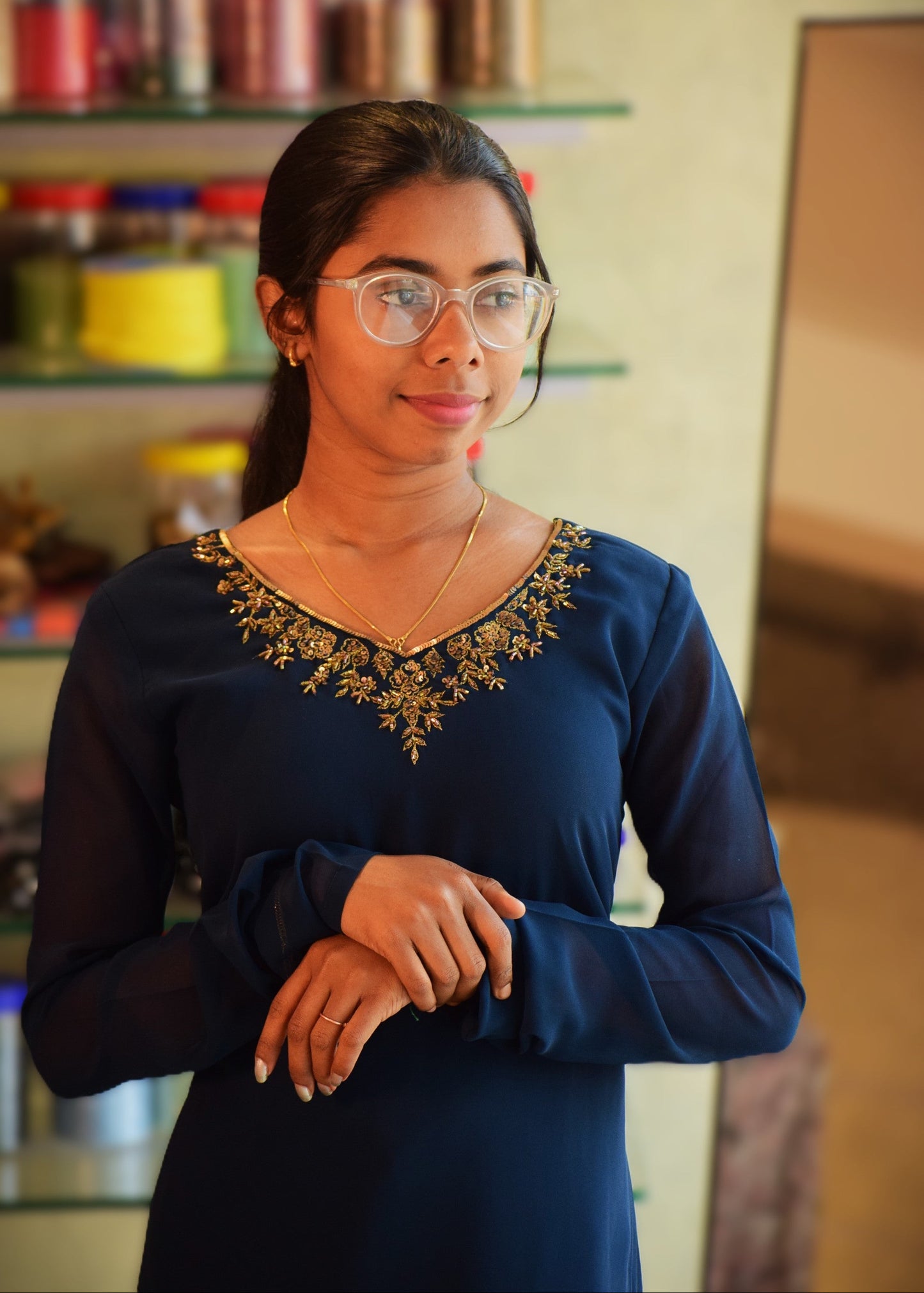 Woman wearing glasses and a blue dress with intricate detailing in a kitchen setting