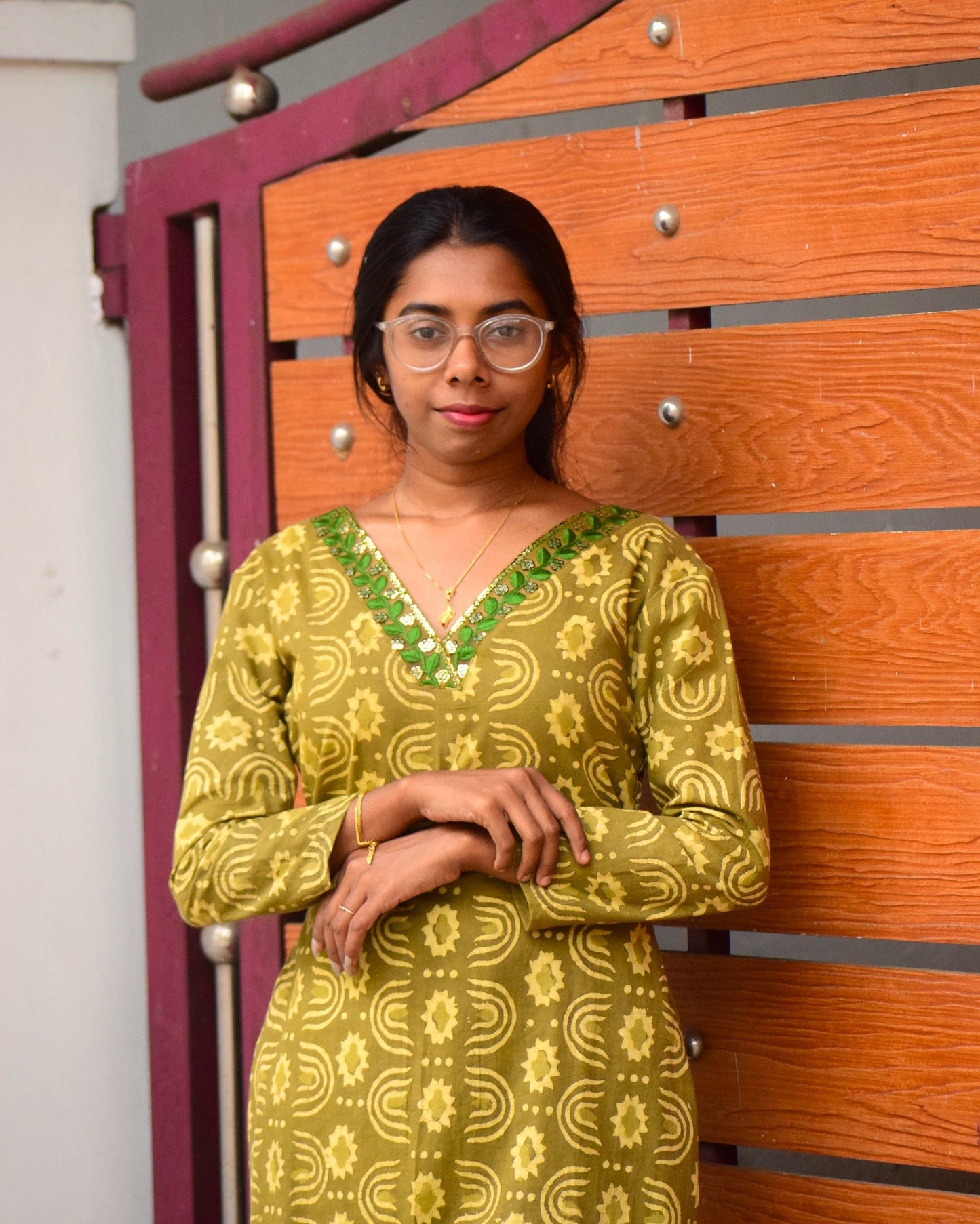 Woman in a green patterned dress standing in front of a wooden gate.