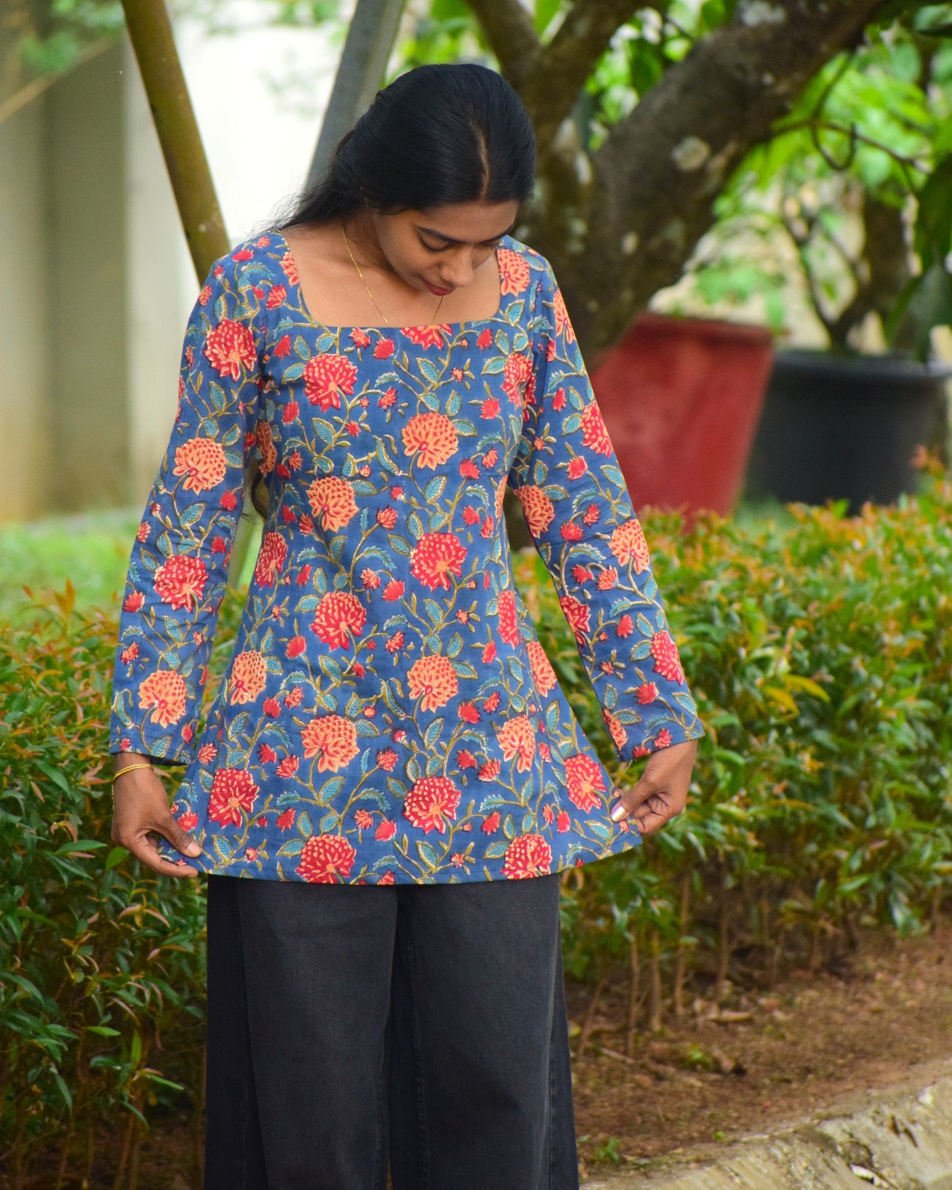 Woman wearing a blue floral top standing outdoors with greenery in the background