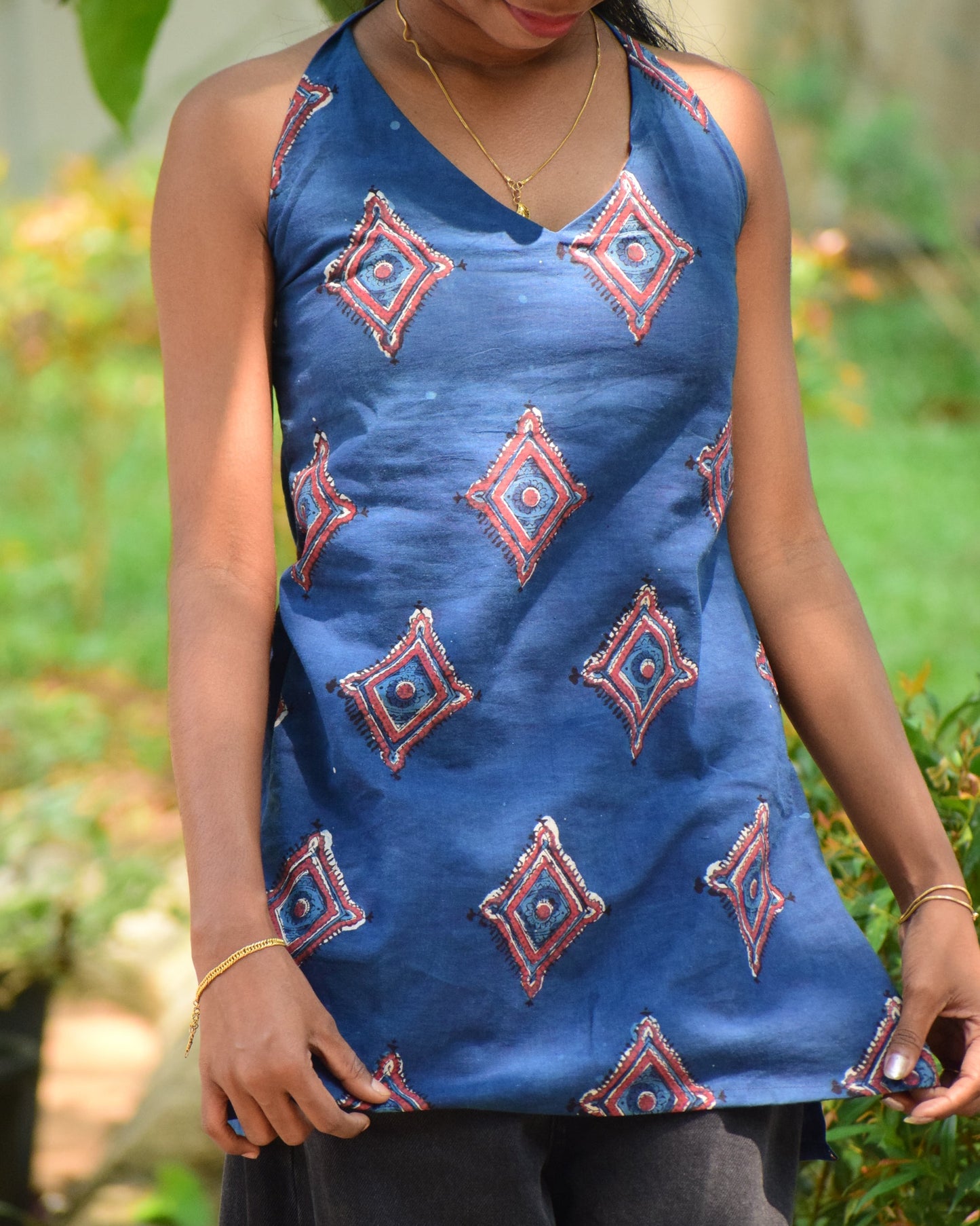 Person wearing a blue traditional outfit with intricate patterns, standing against a blurred natural background.