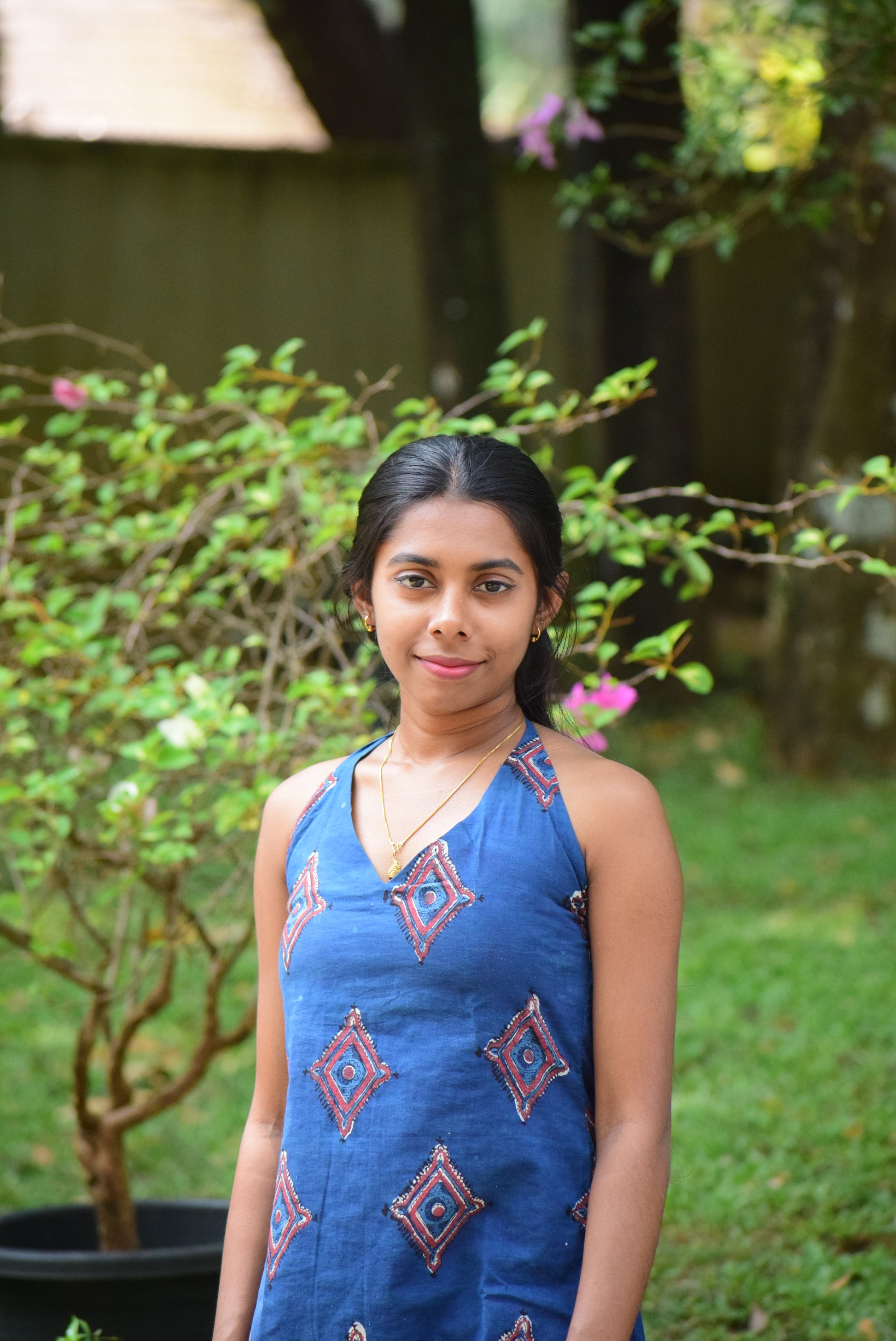 Woman in a blue dress standing outdoors with greenery in the background