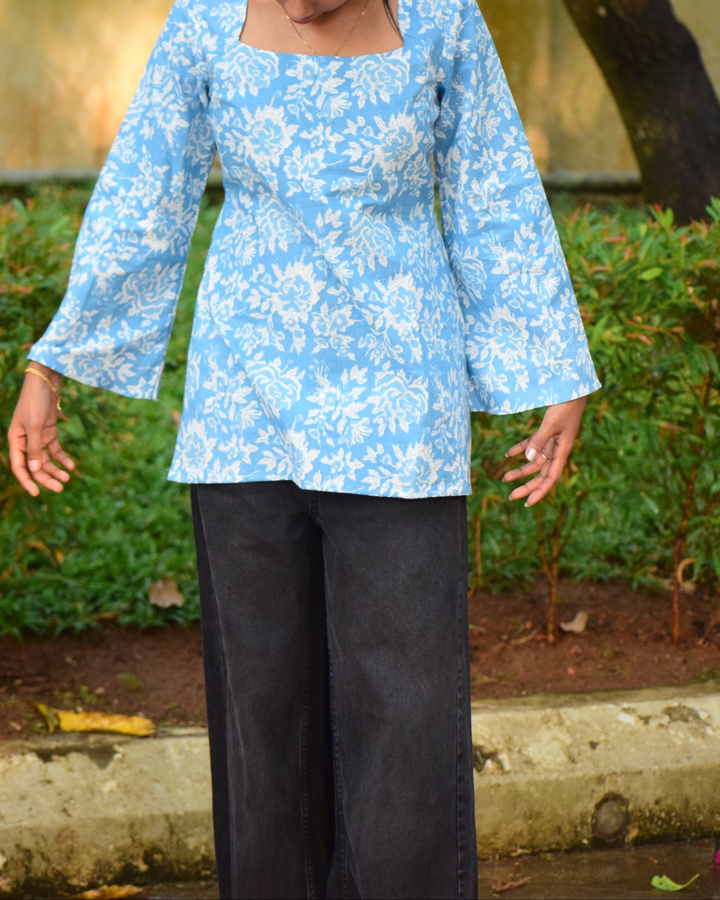 Person wearing a light blue floral dress with dark pants outdoors.