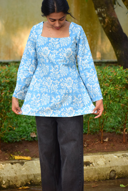 Person wearing a blue floral dress standing outdoors with greenery in the background