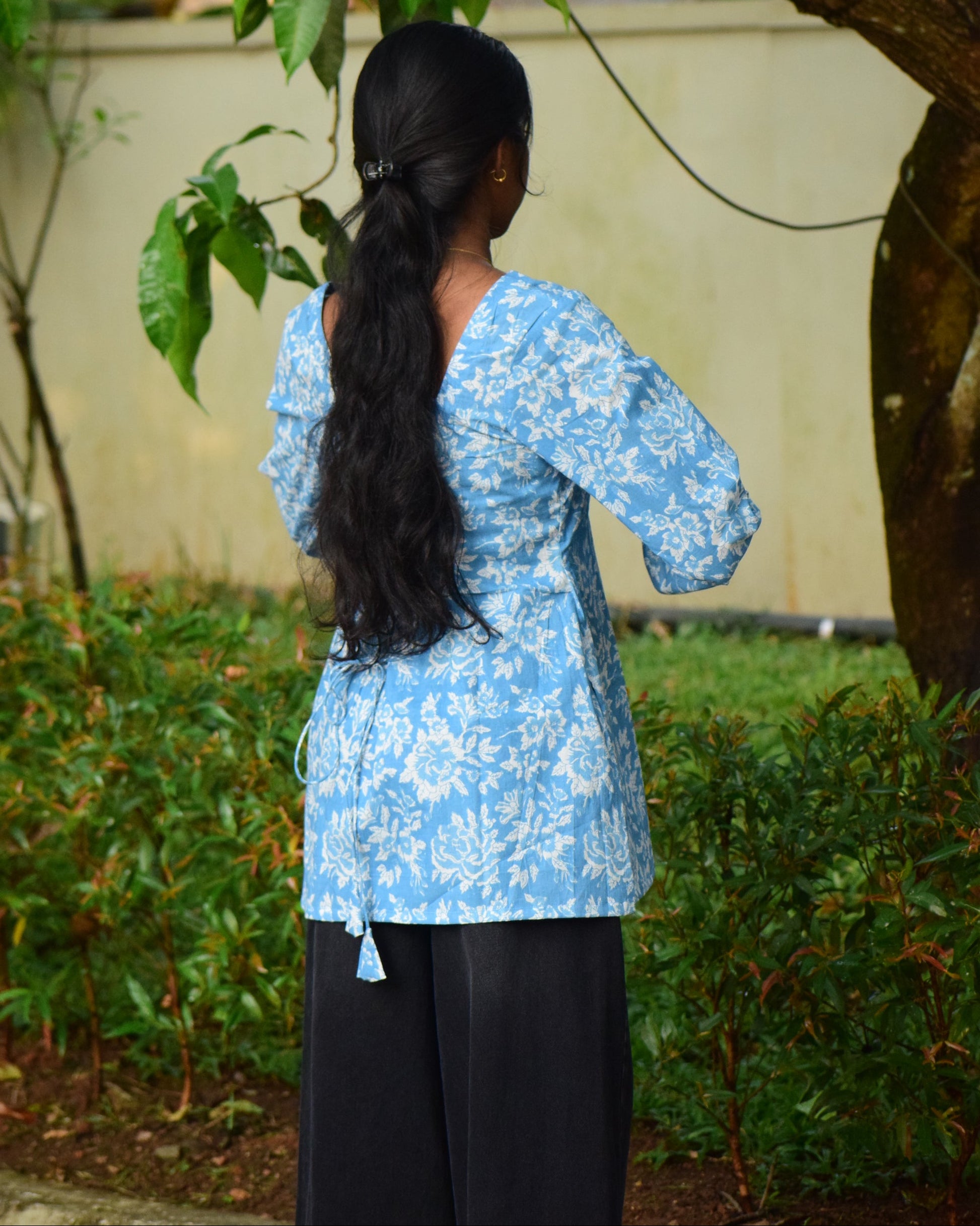 Person wearing a blue floral dress standing among green foliage