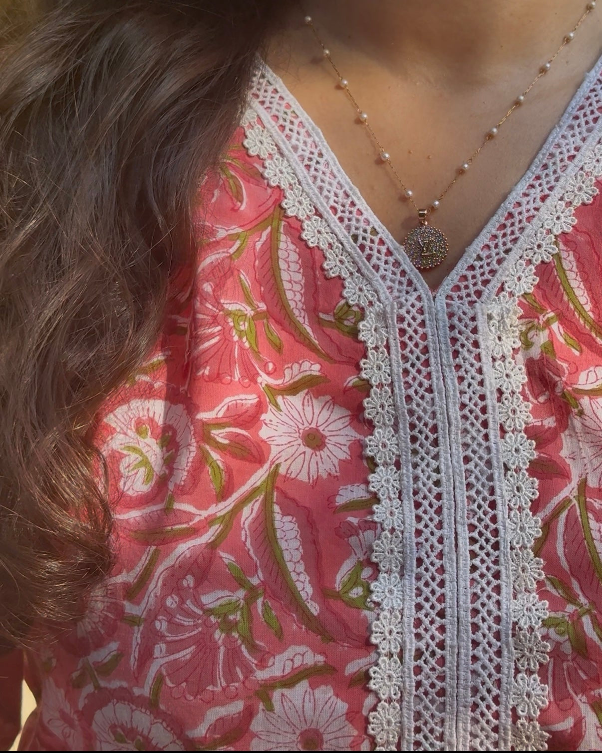 Close-up of a person wearing a pink floral blouse with lace details and a necklace.
