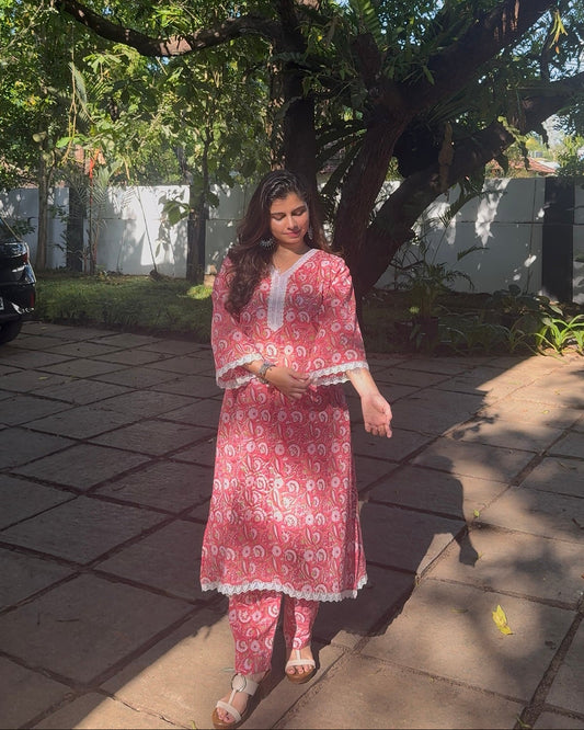 Woman in a pink traditional outfit standing outdoors under a tree.