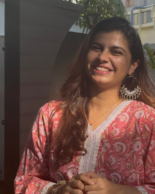 Woman wearing a pink patterned outfit with large hoop earrings, standing outdoors.