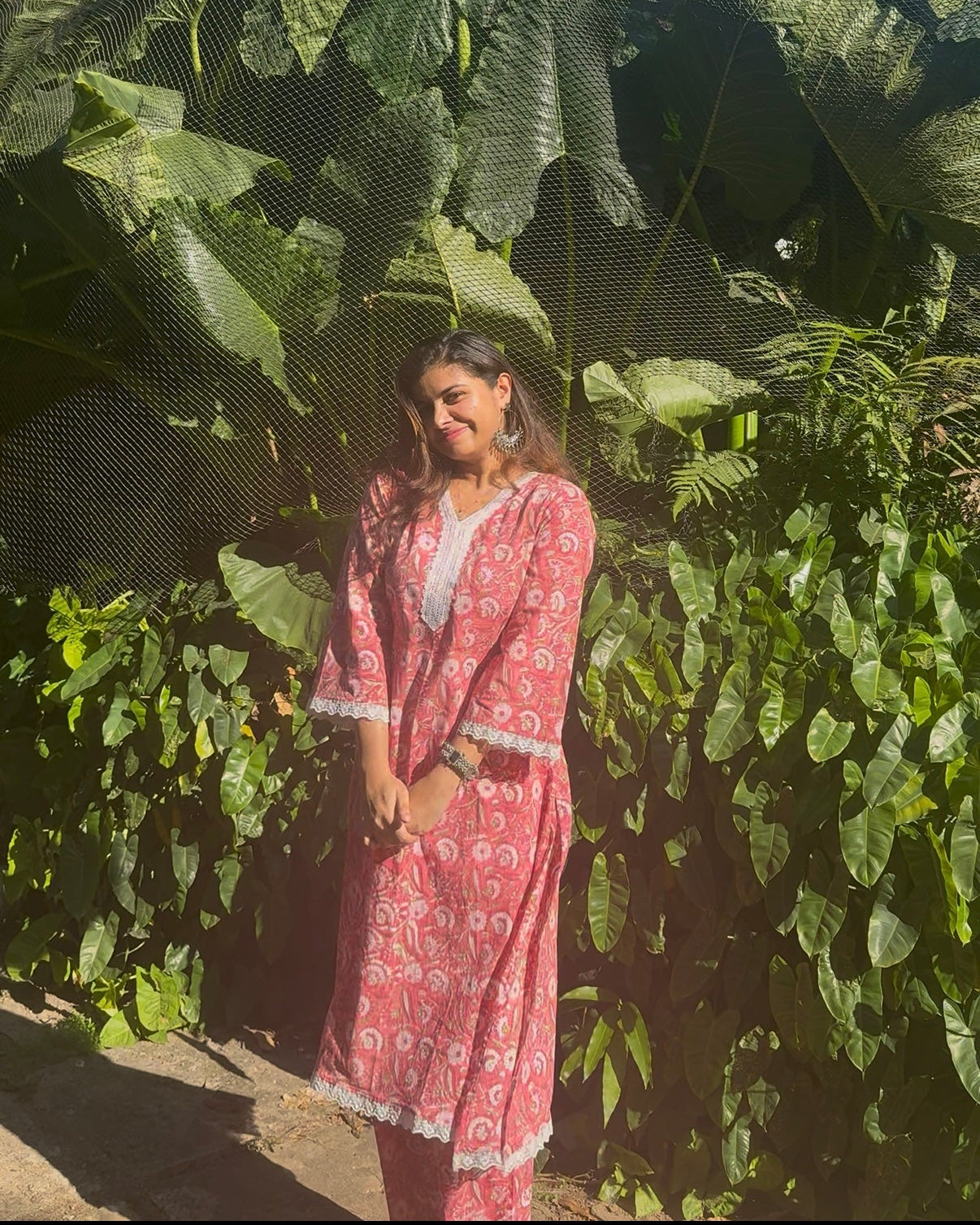 Woman in a pink dress standing in front of large green leaves