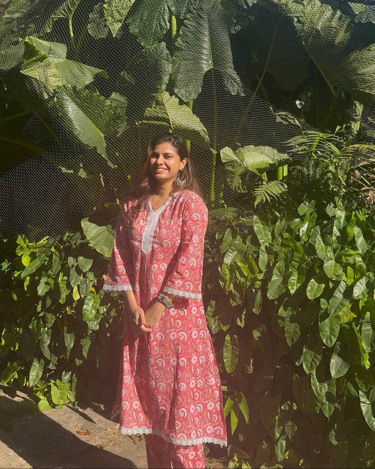 Woman in a pink outfit standing in front of large green leaves