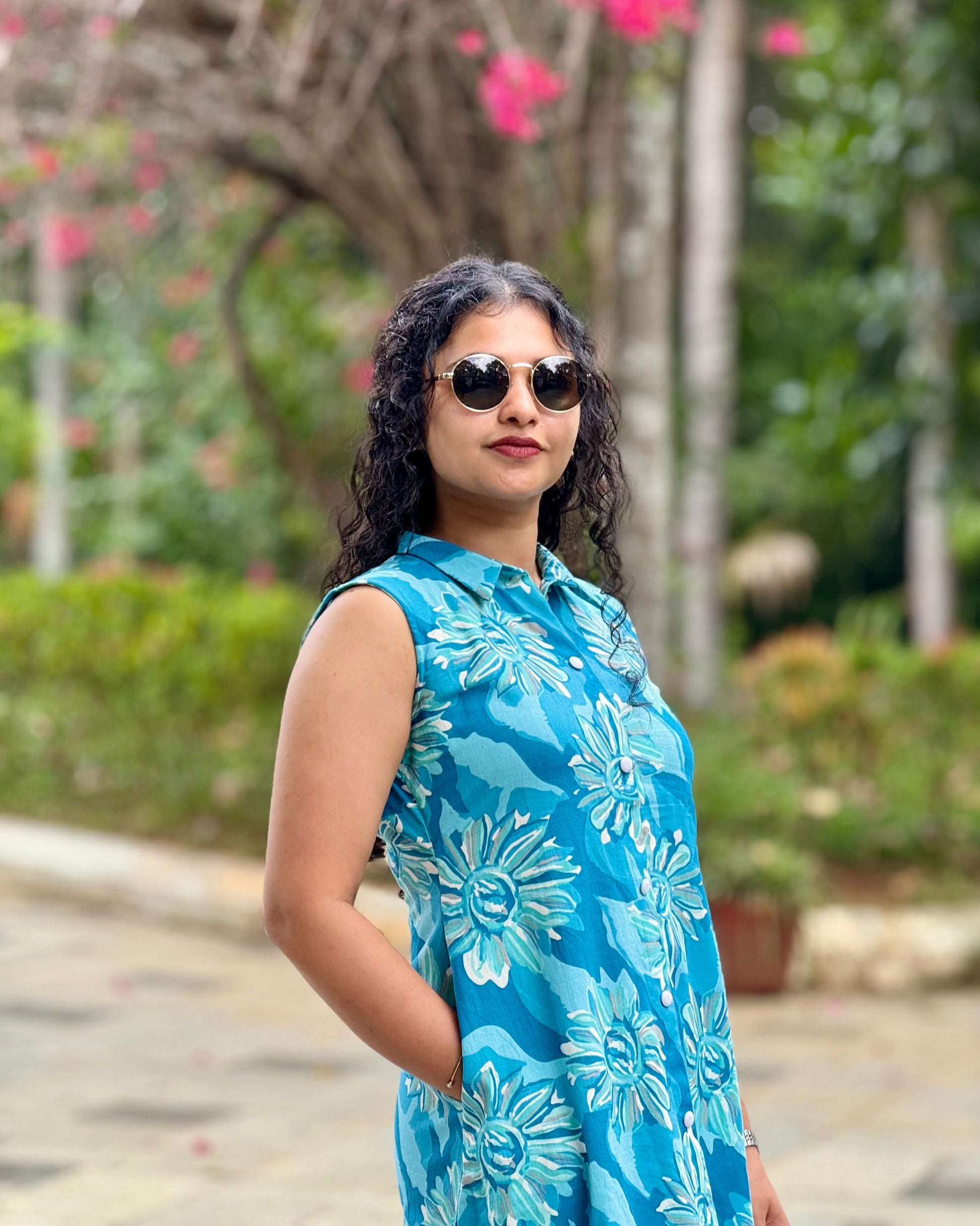 Woman wearing a blue floral dress and sunglasses in a garden setting