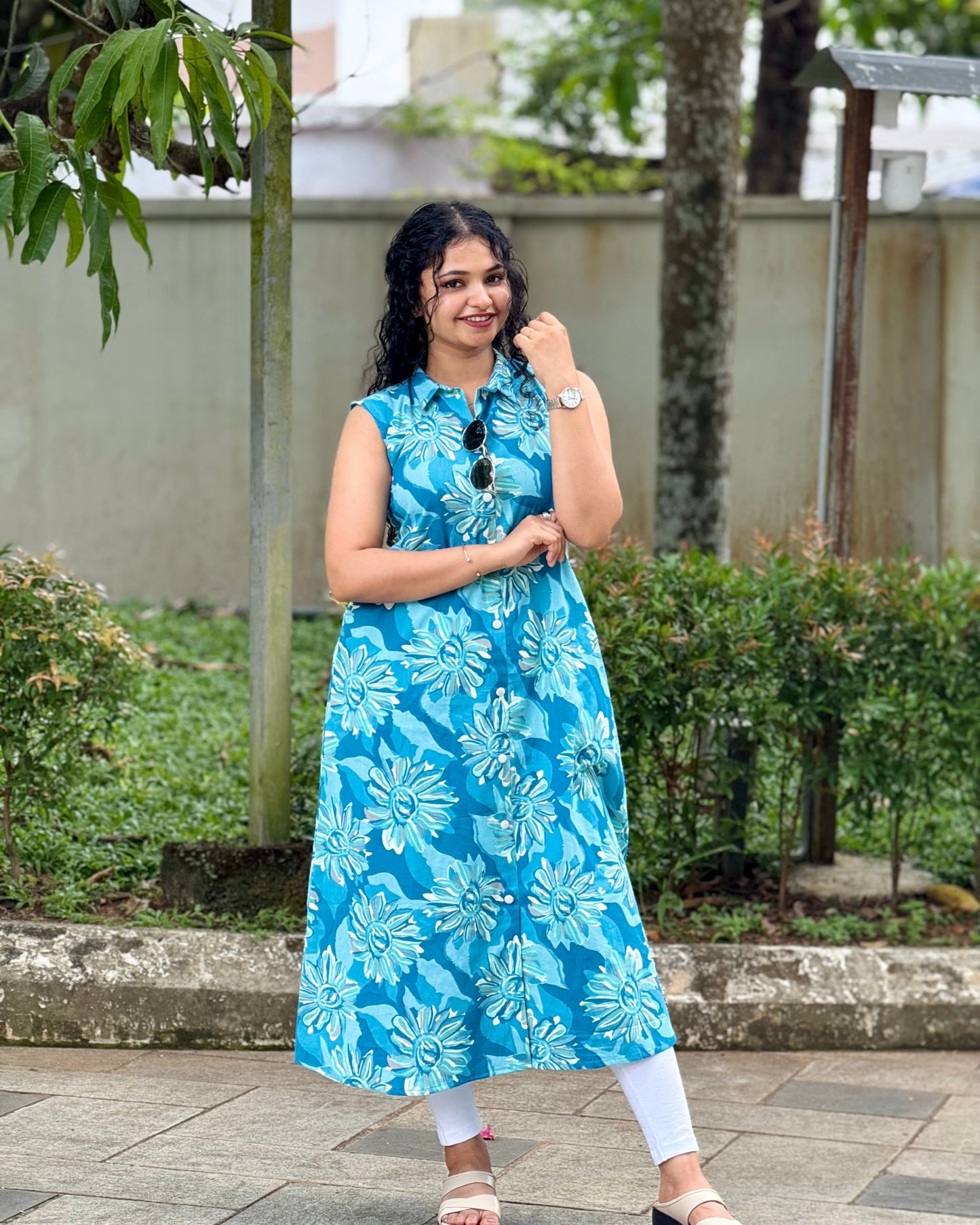 Woman wearing a blue floral dress standing outdoors with greenery in the background