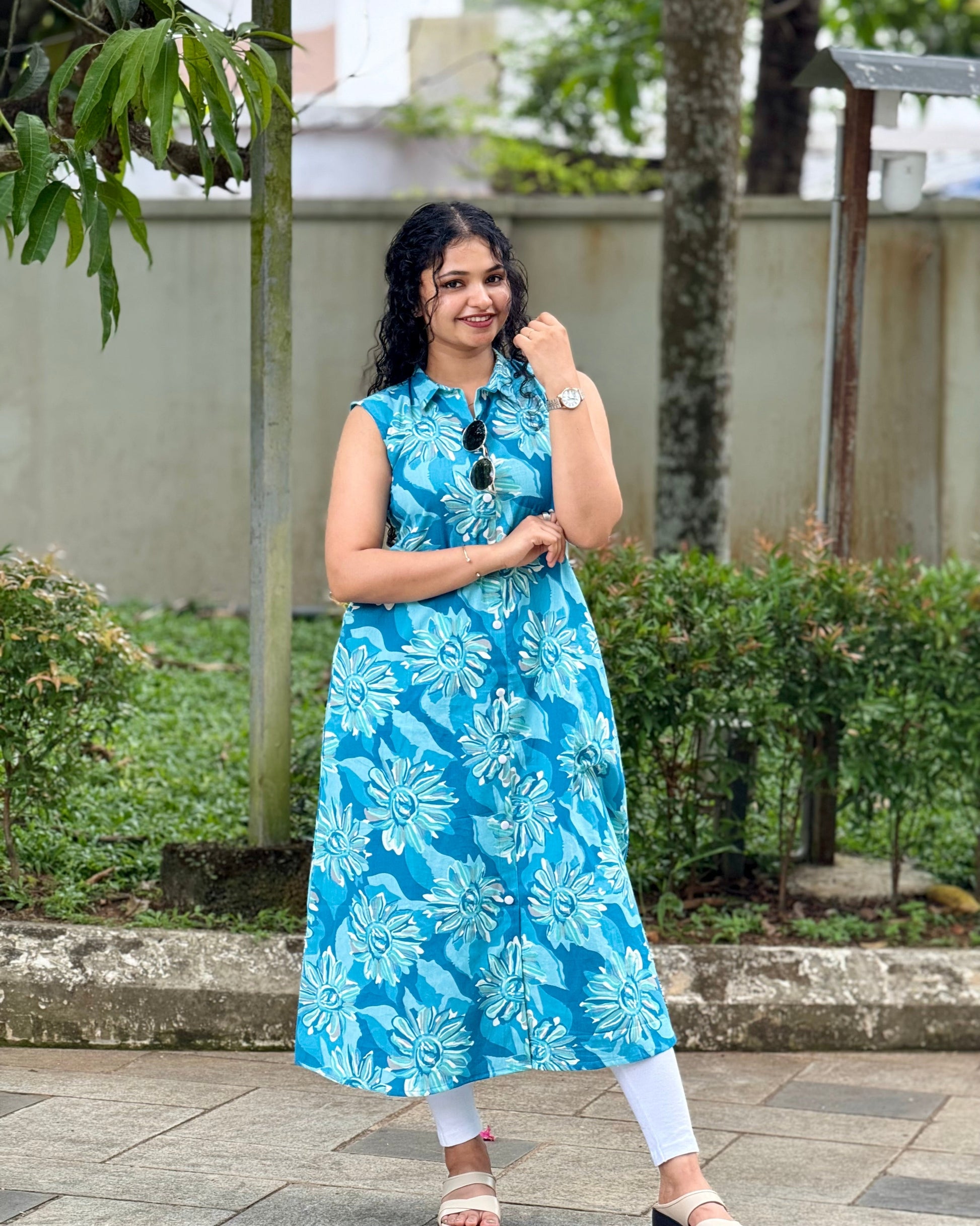 Woman wearing a blue floral dress standing outdoors with greenery in the background