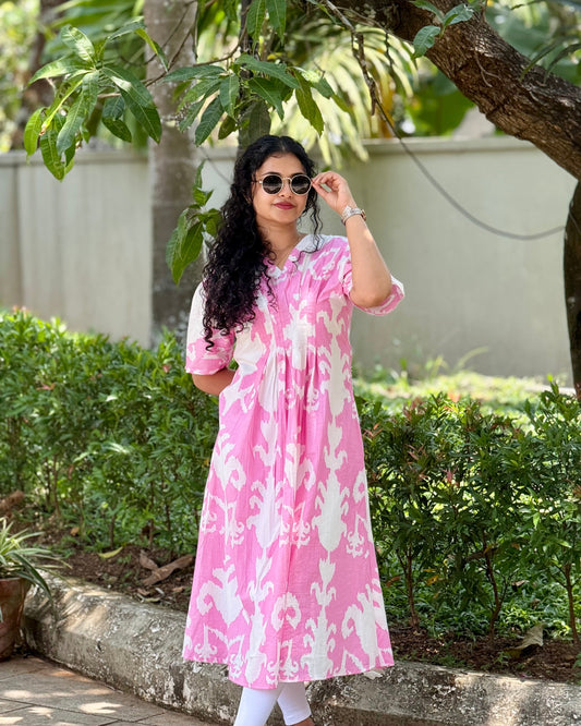 Woman wearing a pink and white patterned dress standing outdoors with greenery in the background