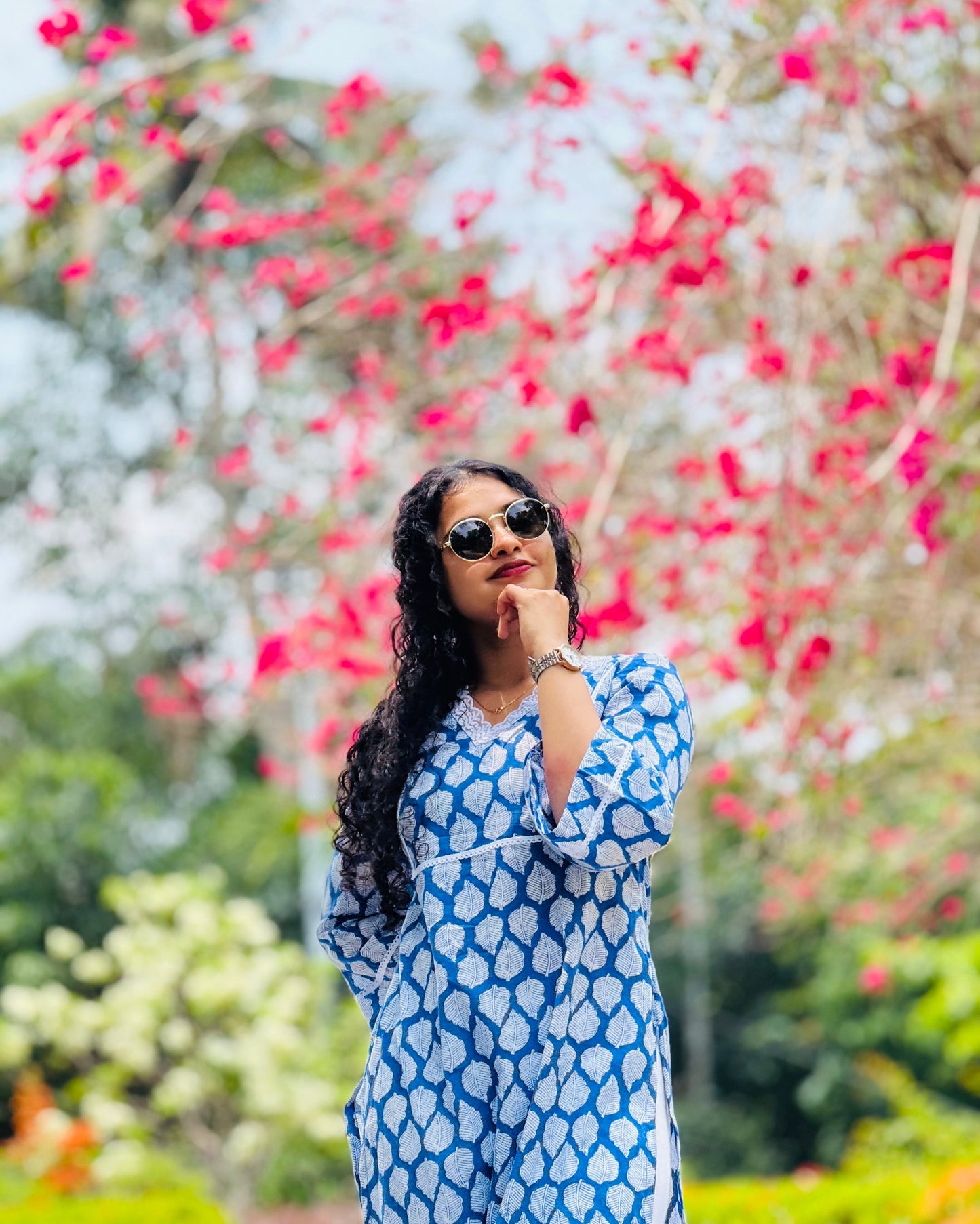 Woman in a blue dress standing in front of pink and white flowers