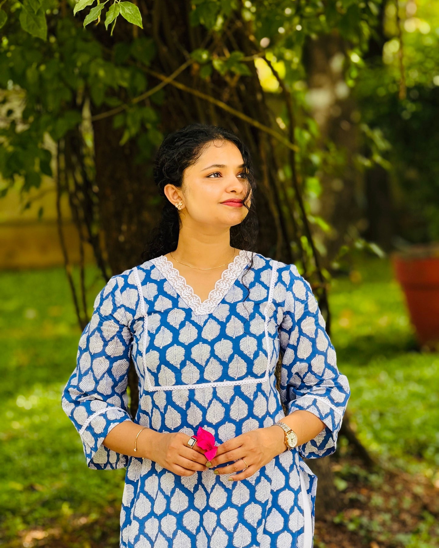 Woman wearing a blue and white patterned dress standing outdoors with greenery in the background