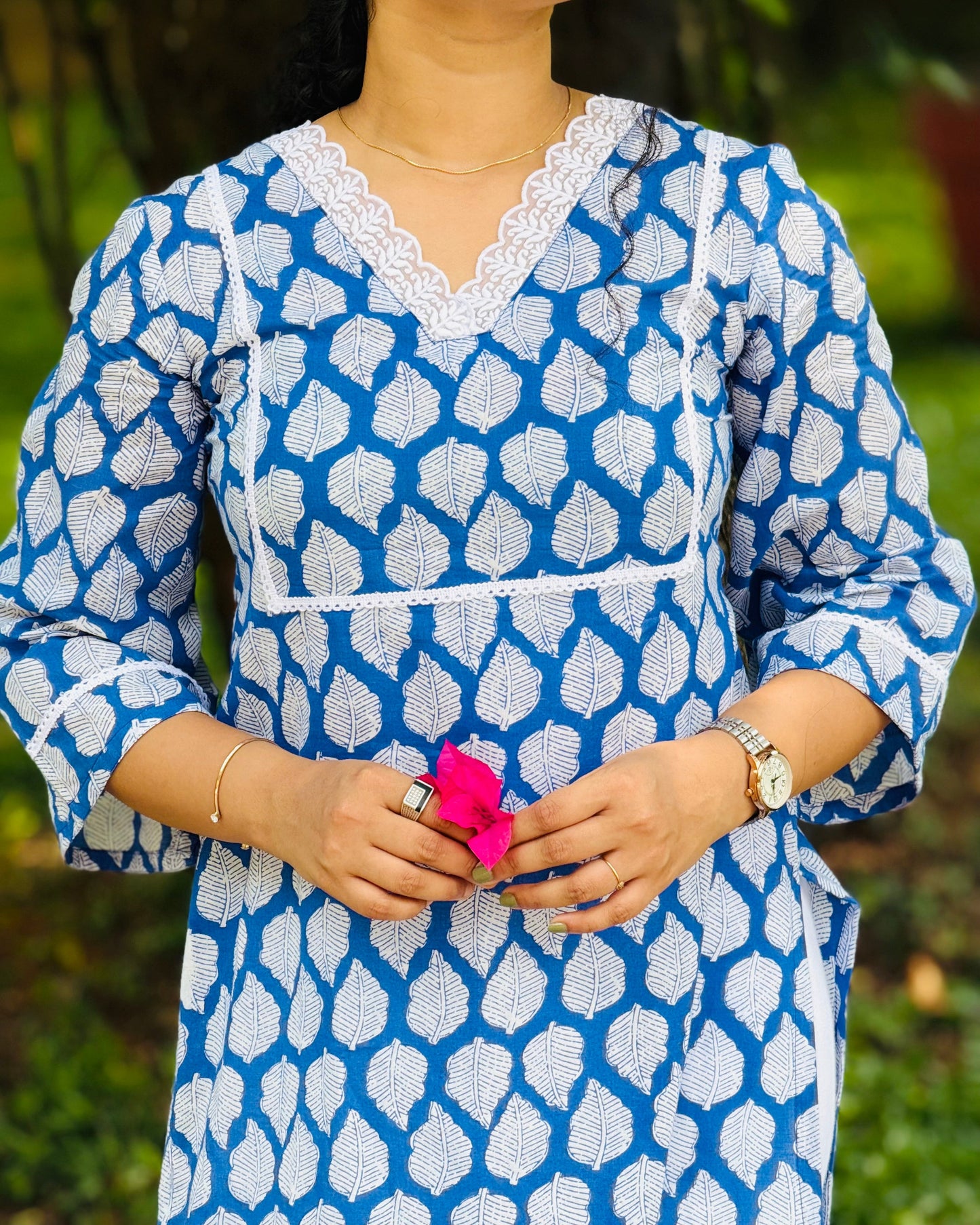 Person wearing a blue and white patterned dress holding a pink flower against a blurred green background