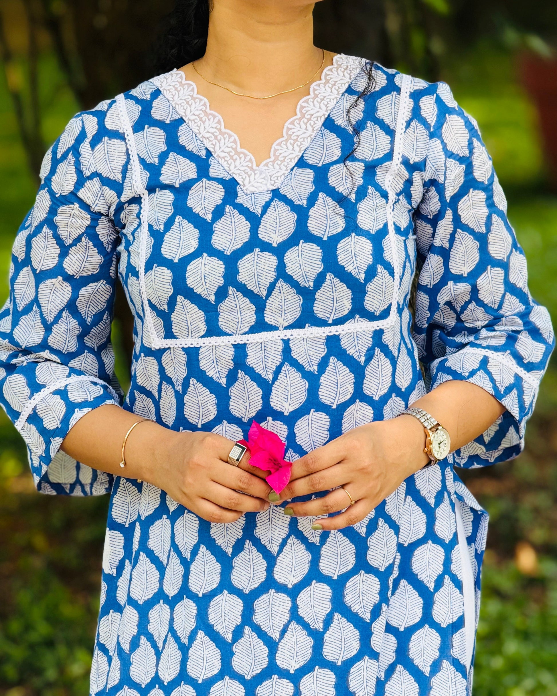 Person wearing a blue and white patterned dress holding a pink flower against a blurred green background