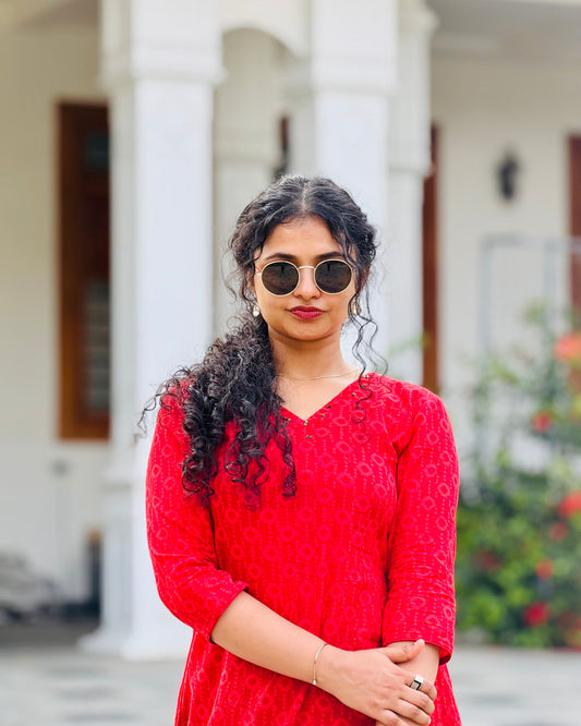 Woman wearing a red patterned top with sunglasses outdoors.