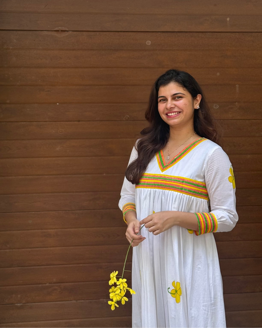 Woman in a white dress with colorful accents holding yellow flowers against a wooden background