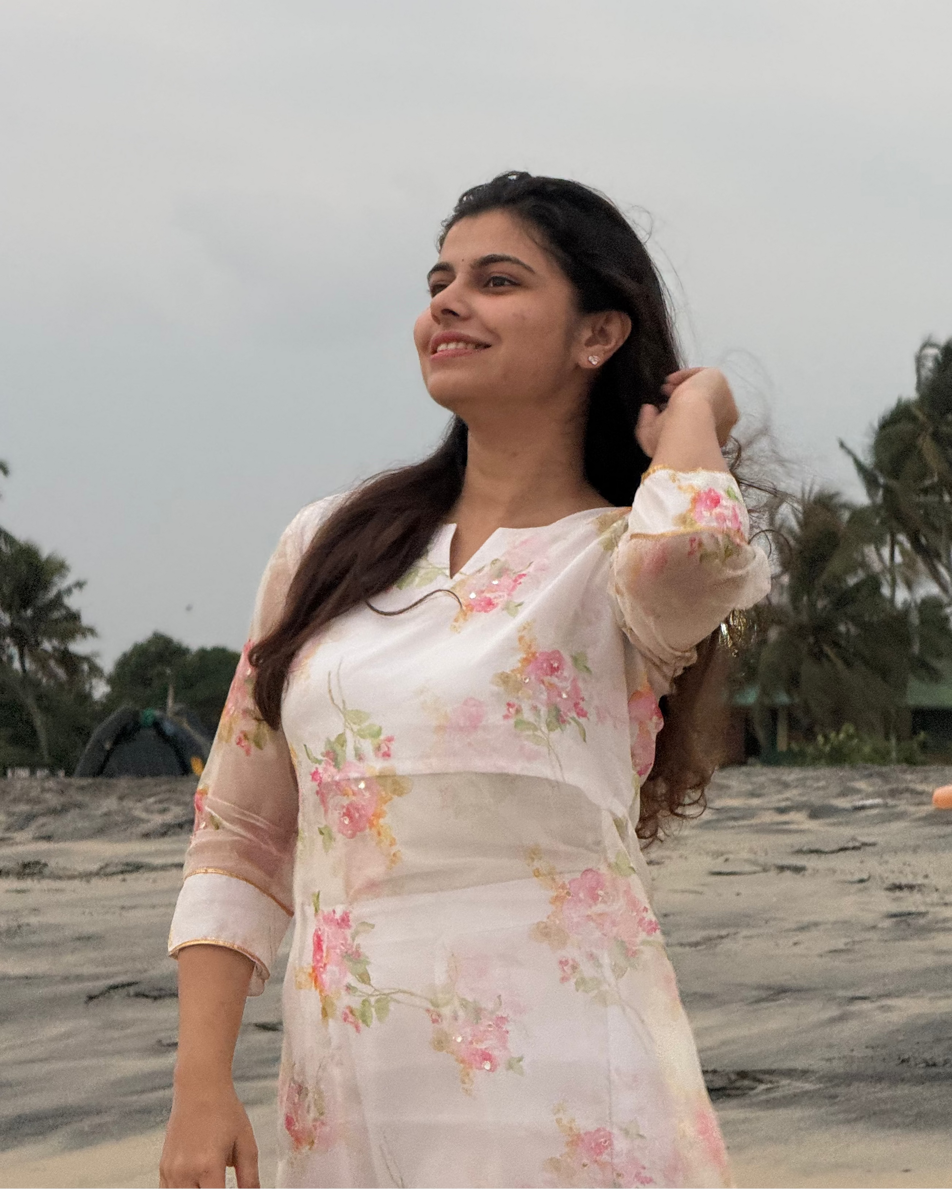 Woman in a floral dress standing on a beach with palm trees in the background