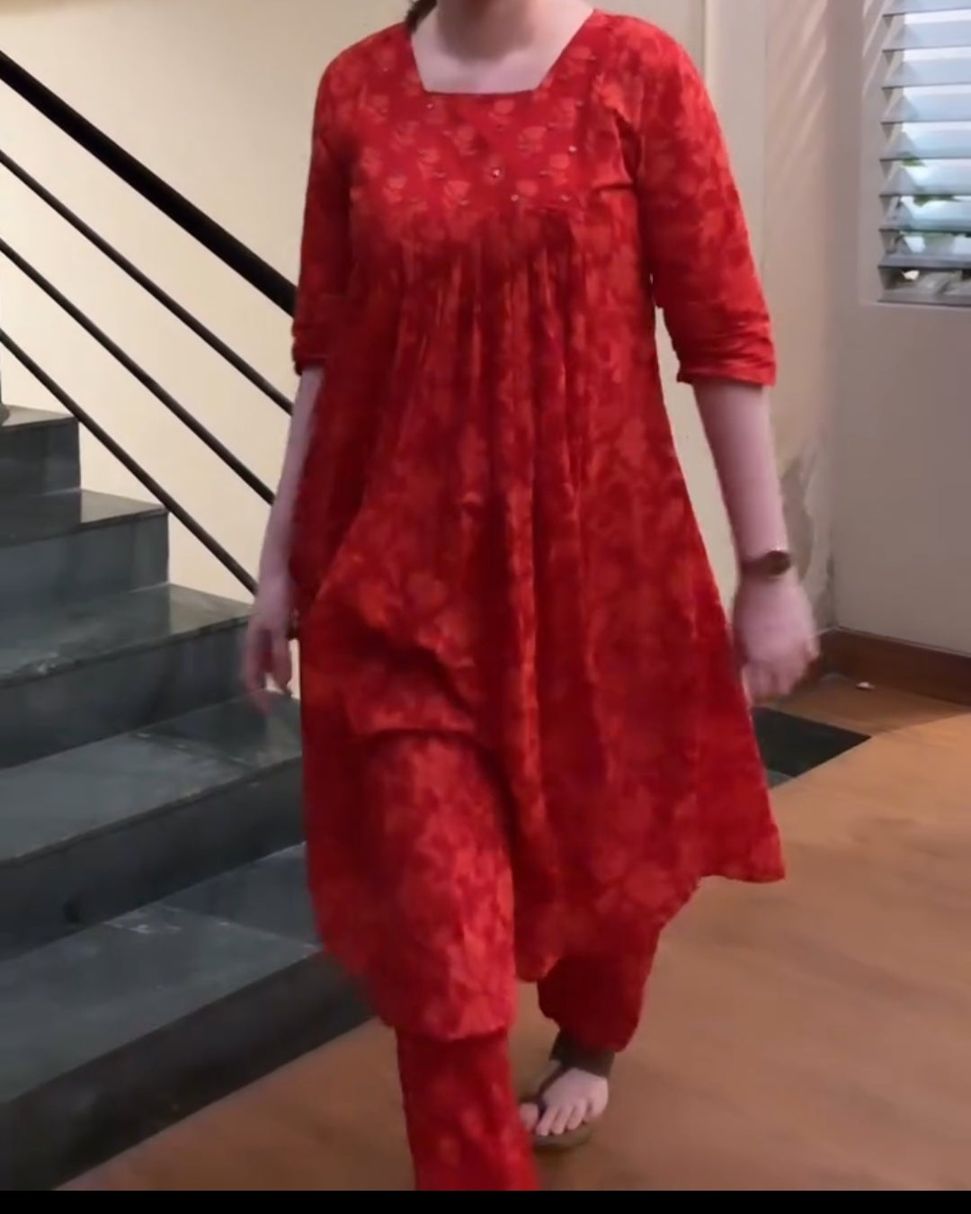 Woman in a red outfit standing on a staircase indoors