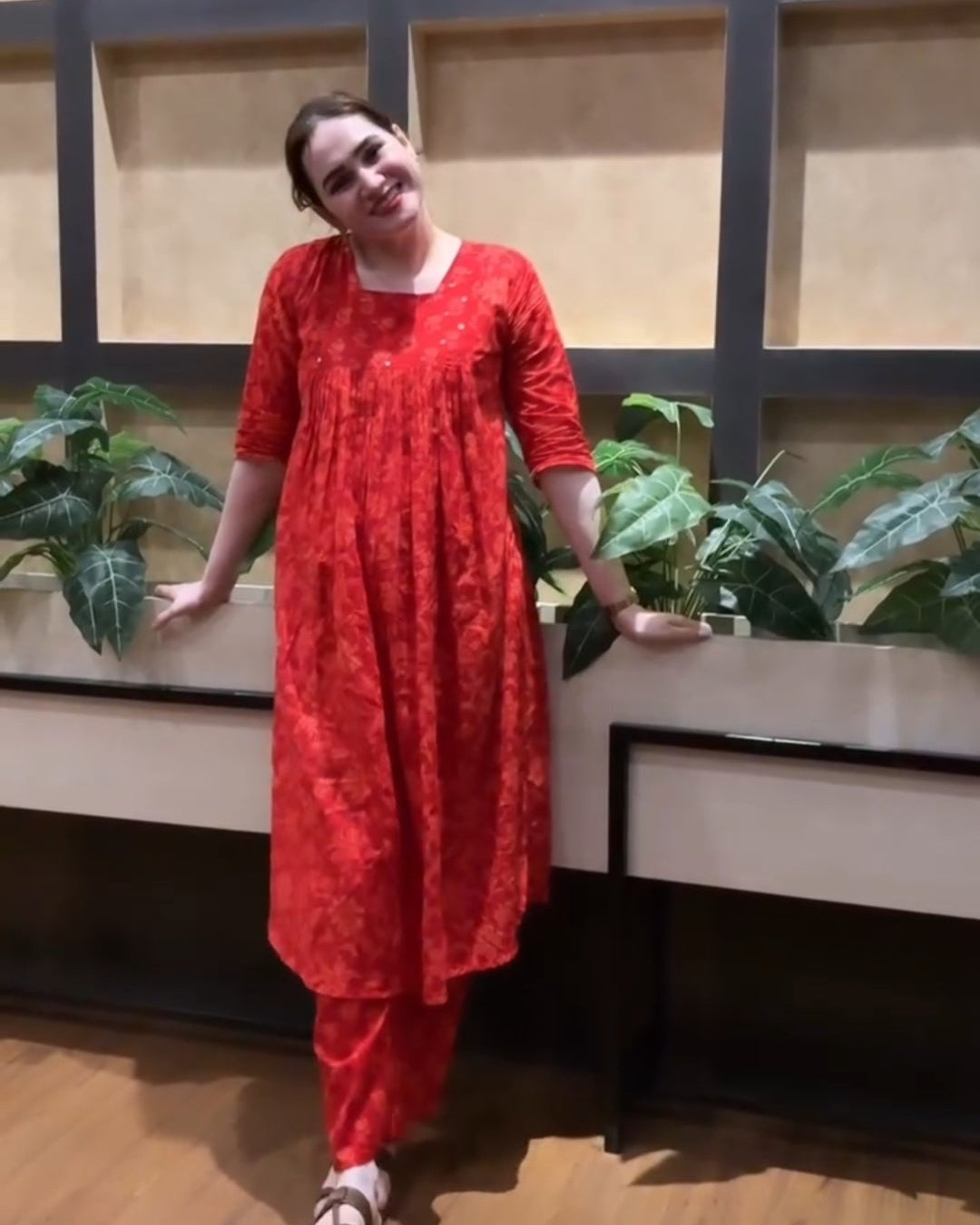 Person wearing a red outfit standing indoors with plants and a wall in the background