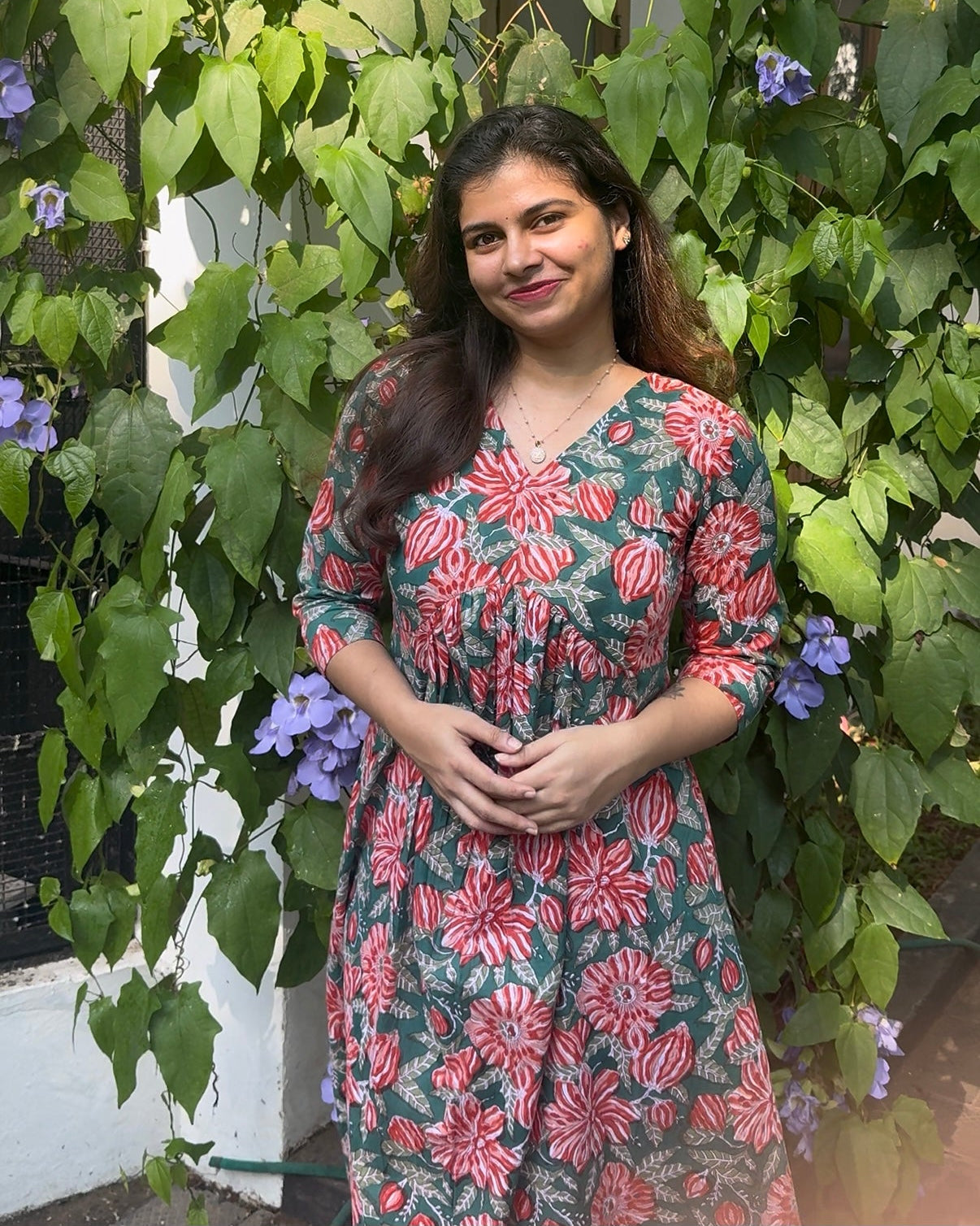 Woman standing in front of green foliage with purple flowers