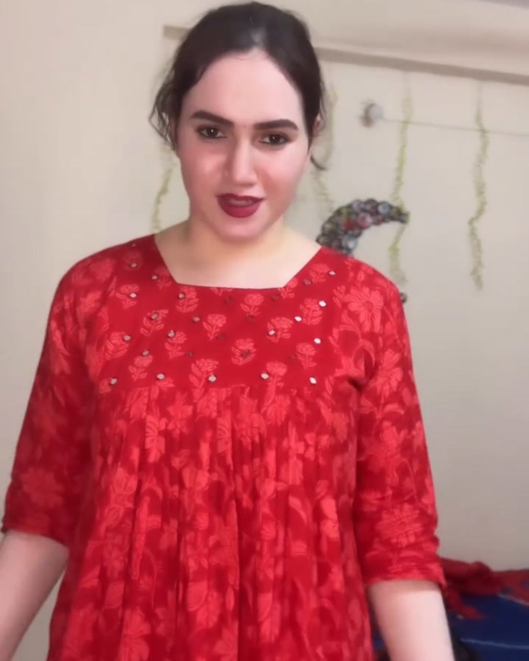 Person wearing a red patterned dress indoors with a neutral background