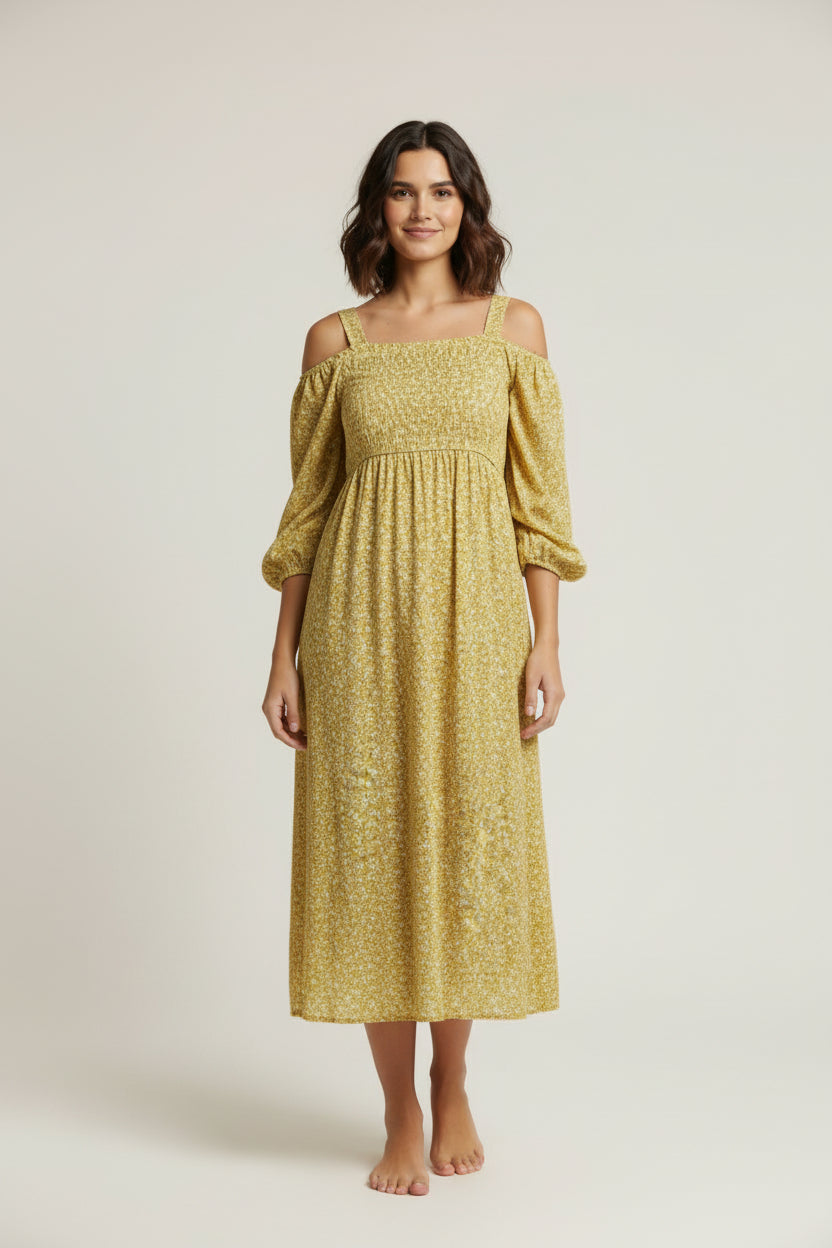 Woman wearing a yellow dress standing in front of a white backdrop with photography equipment around.