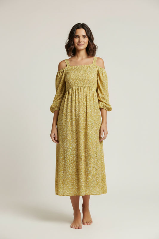 Woman wearing a yellow dress standing in front of a white backdrop with photography equipment around.