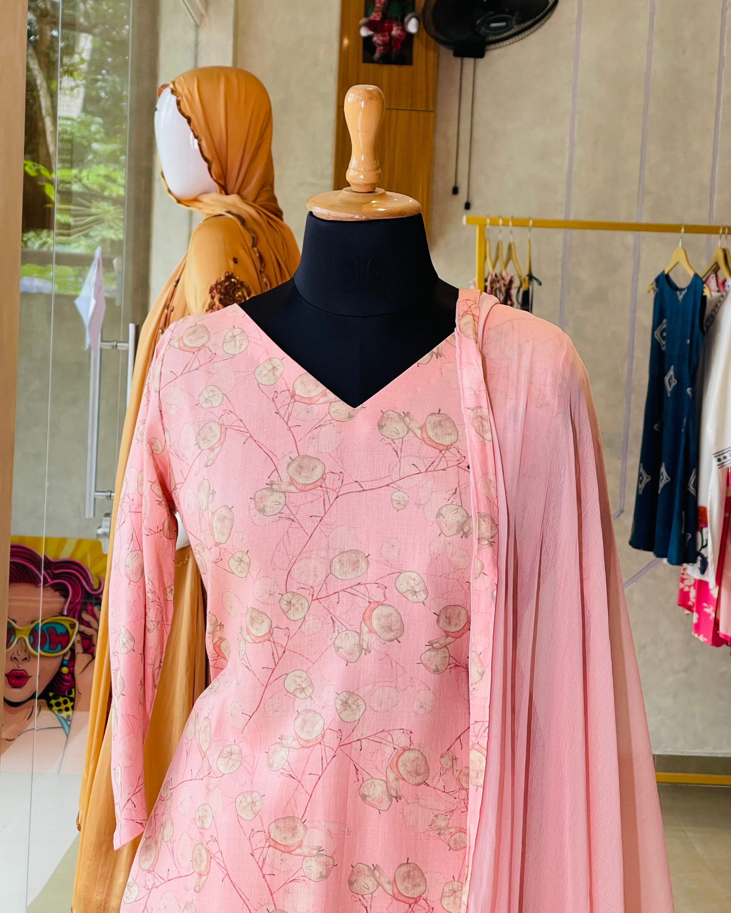 Mannequin wearing a pink floral dress with a matching dupatta in a store setting.