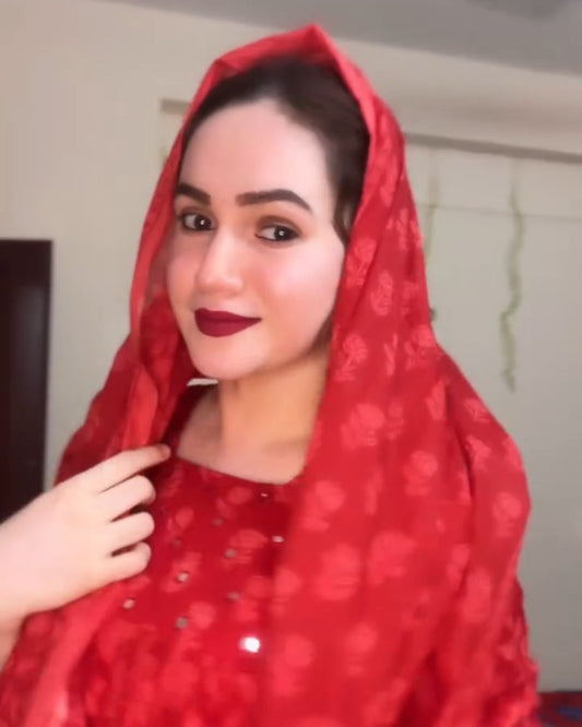 Woman wearing a red headscarf and red outfit indoors.