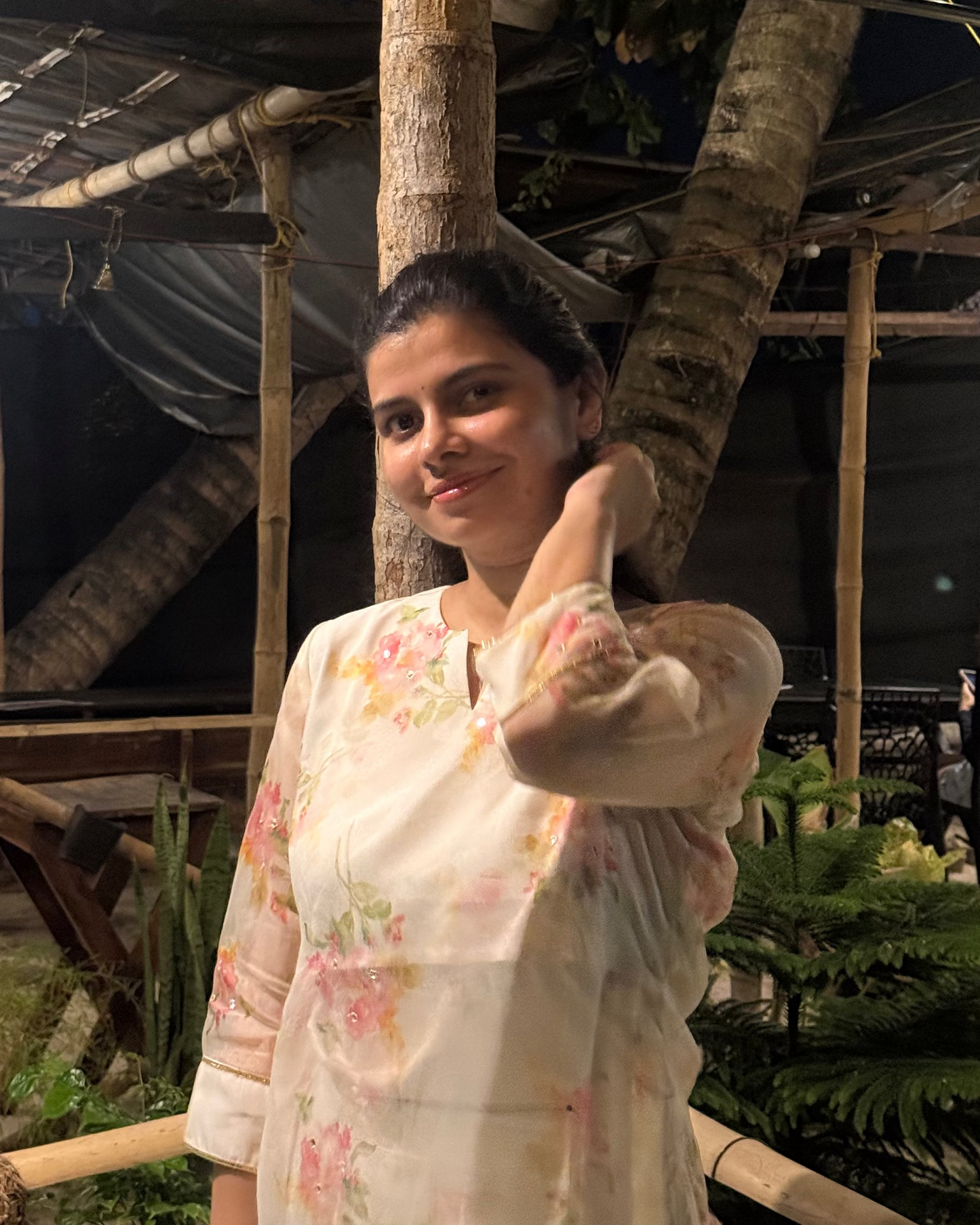 Woman in a floral dress standing under a wooden structure at night.